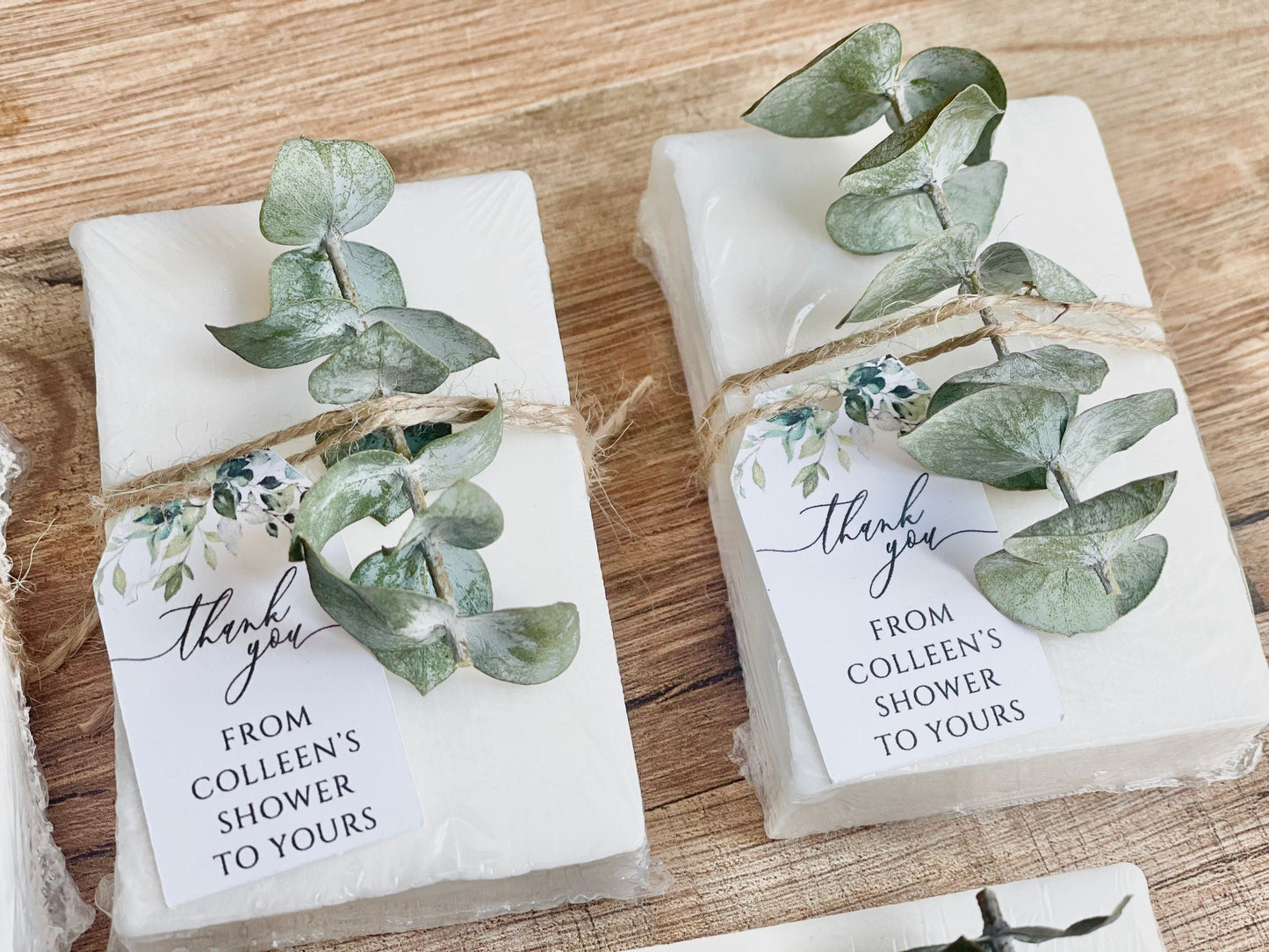 May include: Two white gift boxes wrapped with twine and eucalyptus sprigs. Each box has a thank you tag with the text 'Thank you' in cursive. The tag also includes the text 'From Colleen's Shower To Yours'.